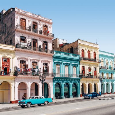 Classic Cuban street scene with brightly coloured buildings and a blue classic convertible car in the sun.